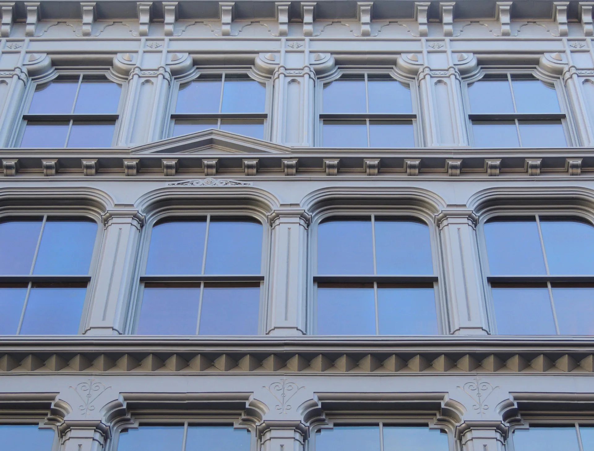 Neoclassical facade with three floors of tall windows framed by fluted columns and cornices, featuring blue-tinted glass and gray stone detailing by Walter B. Melvin Architects.