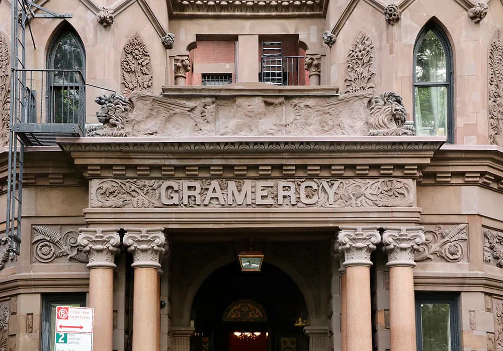 Historic building facade with pink stone, ornamental columns, and arched entrance displaying 'GRAMERCY' signage, restored by Walter B. Melvin Architects.