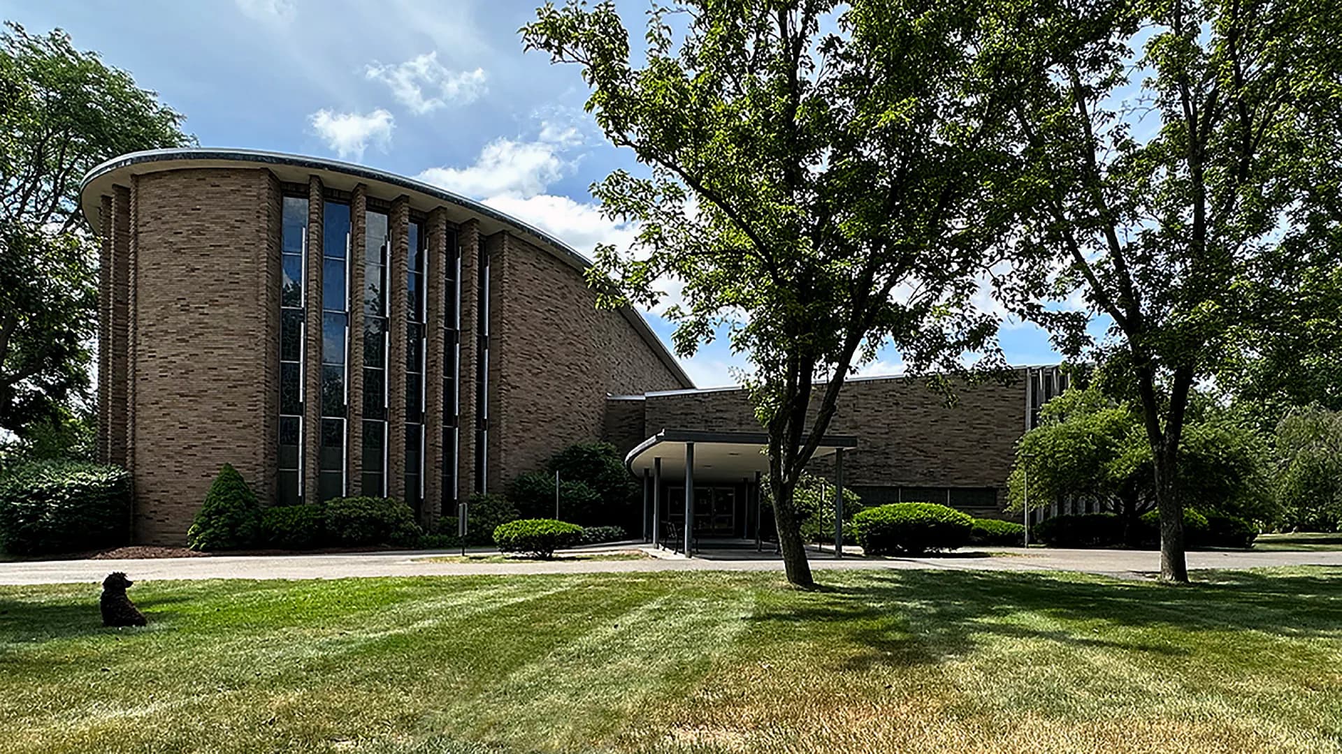 Modernist brick chapel with curved cylindrical tower, vertical window slits, and manicured landscaping by Walter Sedovic Architects.