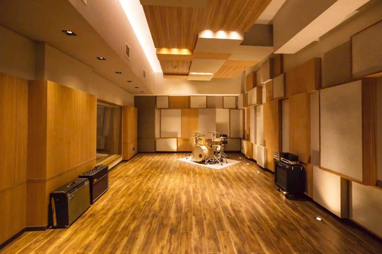 A spacious studio or performance space with warm wood flooring, acoustic paneling on walls, and professional lighting fixtures by Walters-Storyk Design Group.