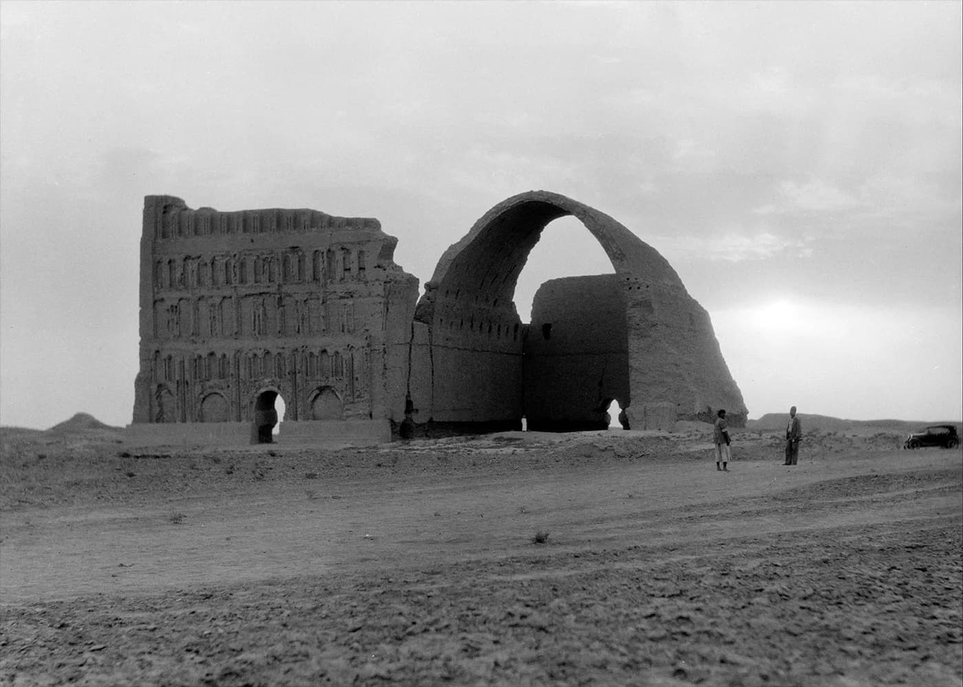 Stark desert landscape with brutalist concrete structures featuring geometric arches and rectangular forms, photographed in black and white by Wartel.
