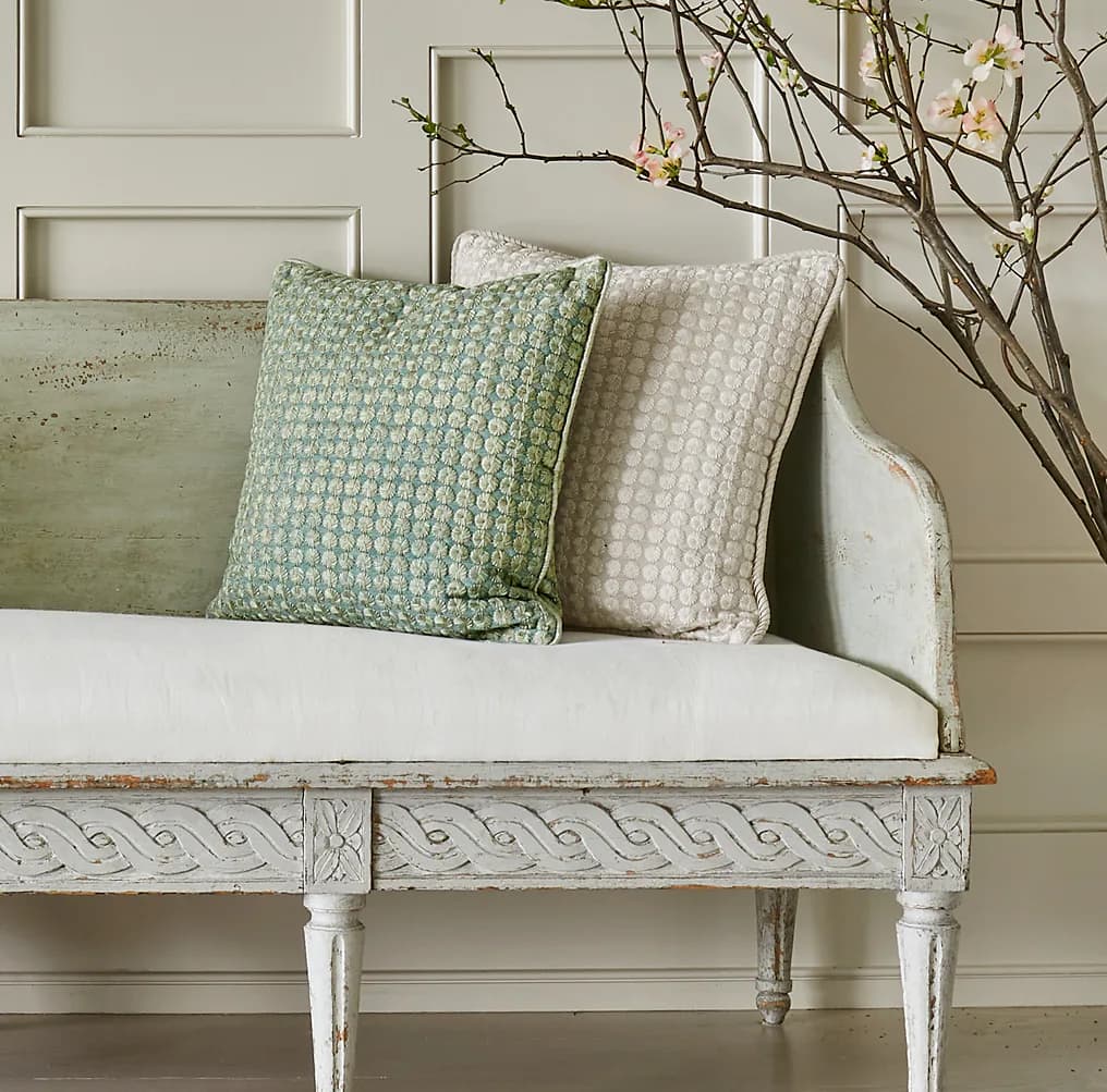 Pale whitewashed wooden bench with green and cream patterned pillows and dried branches, designed by Weitzner Limited.