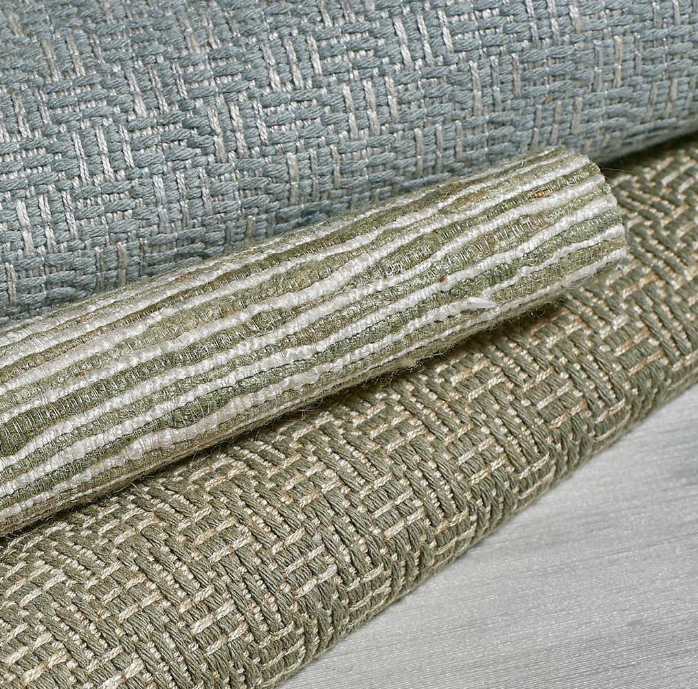 Close-up detail of layered upholstered textiles in neutral greens and creams with decorative trim, showcasing fabric selection and material composition by Weitzner Limited.