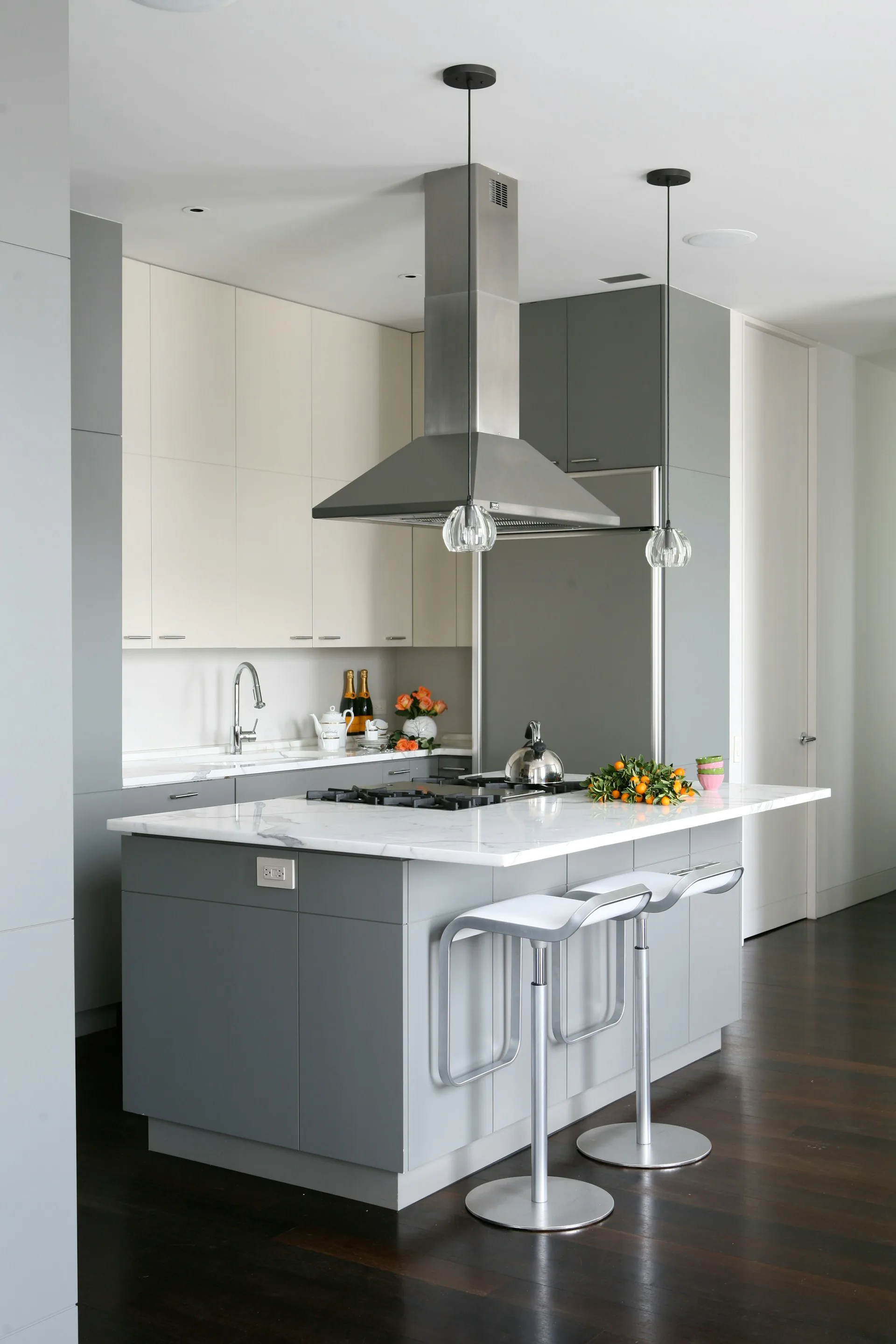 Modern kitchen with gray and white cabinetry, white quartz countertop, stainless steel appliances, and pendant lighting over the island by Wettling Architects.
