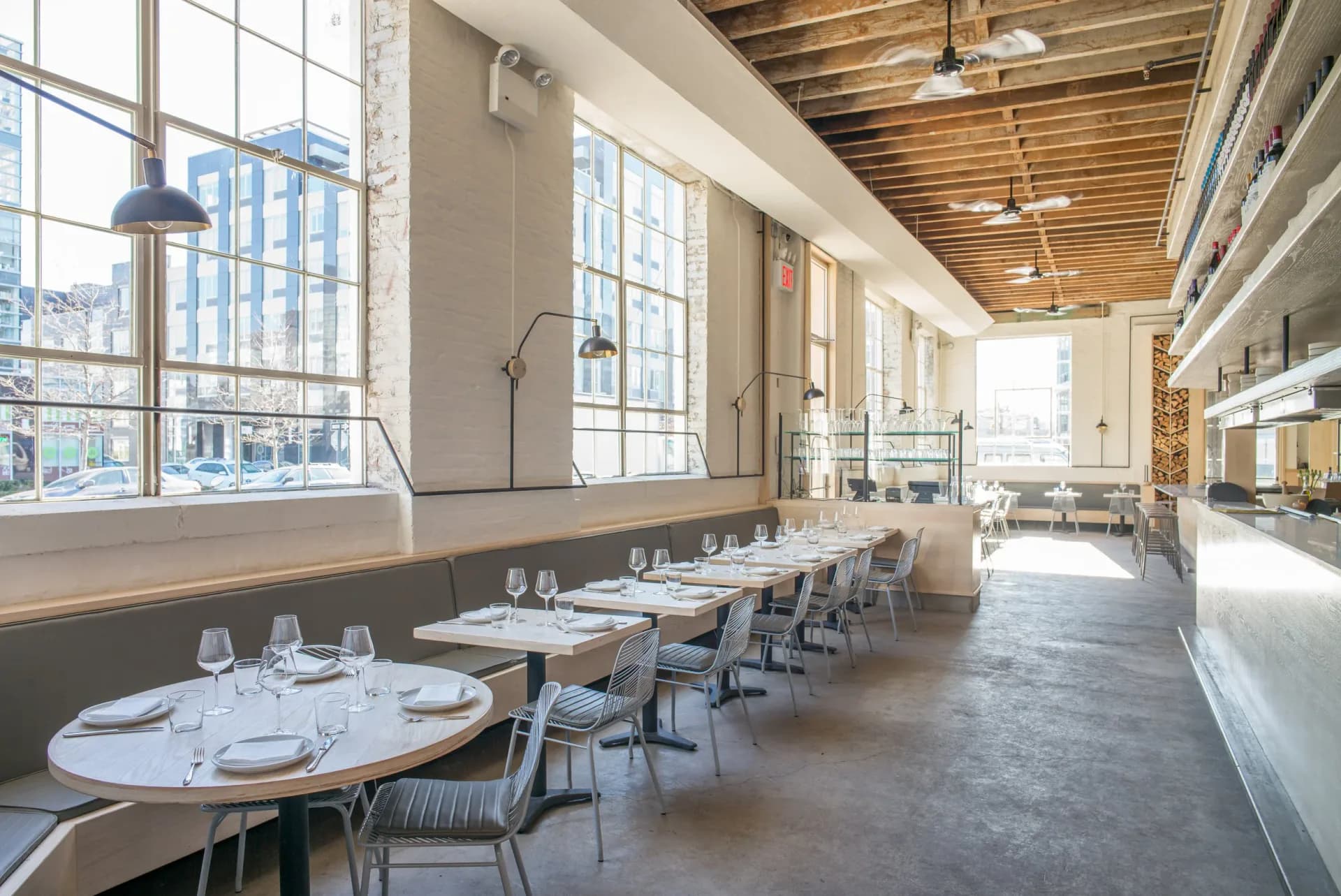 Modern restaurant interior with long dining tables, floor-to-ceiling windows, exposed wooden ceiling, and minimalist furnishings by Withers Studio.