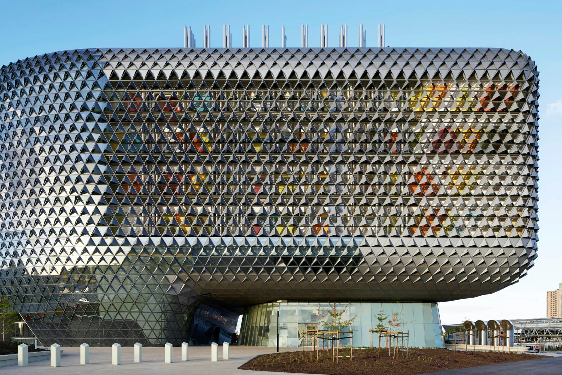 Modern curved building with distinctive diamond-patterned metallic facade and protruding structural elements, photographed in daylight by Woods Bagot.