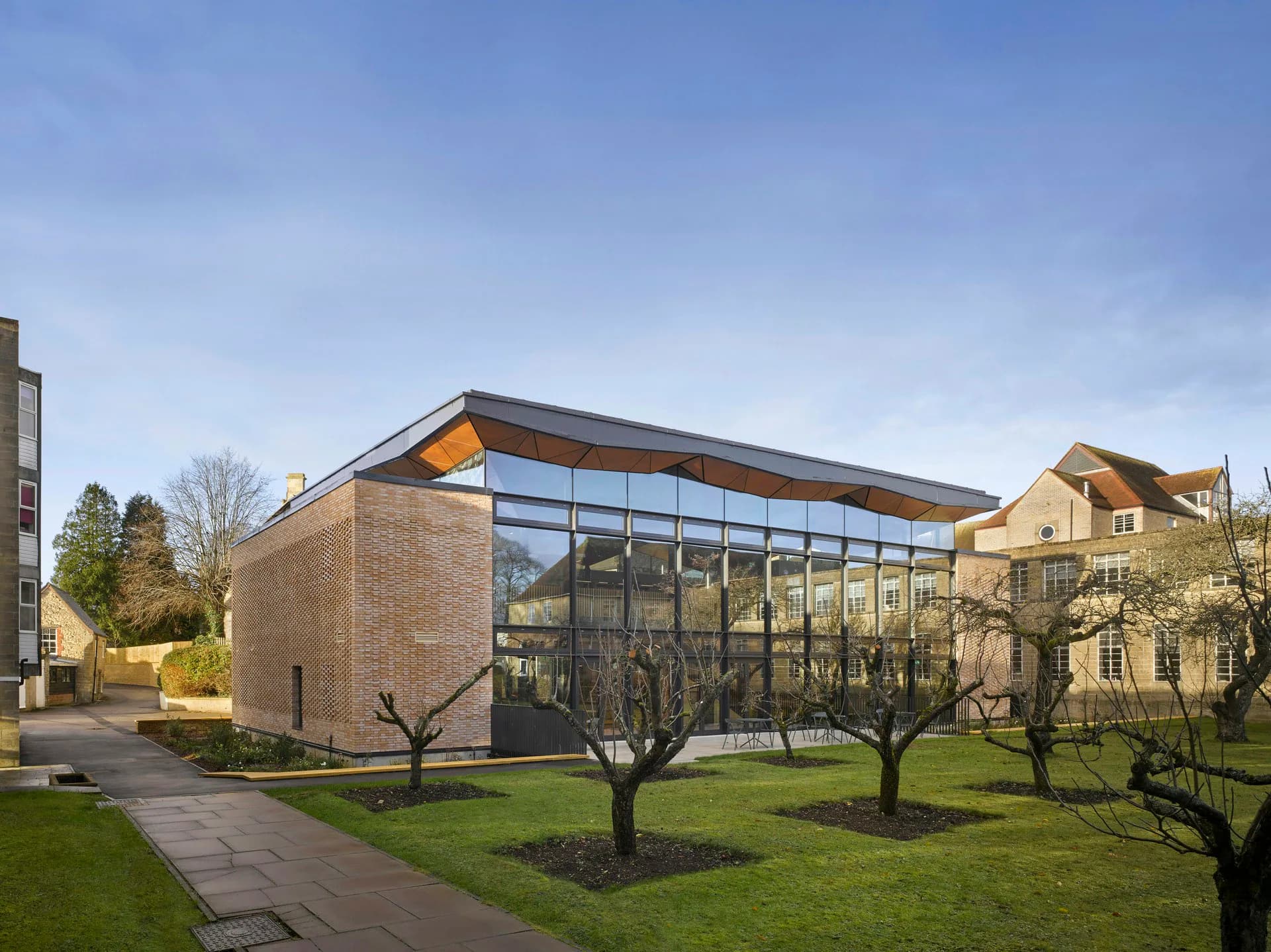 Modern brick and glass building with sloped roof set among bare trees on manicured lawn, designed by Woods Bagot.