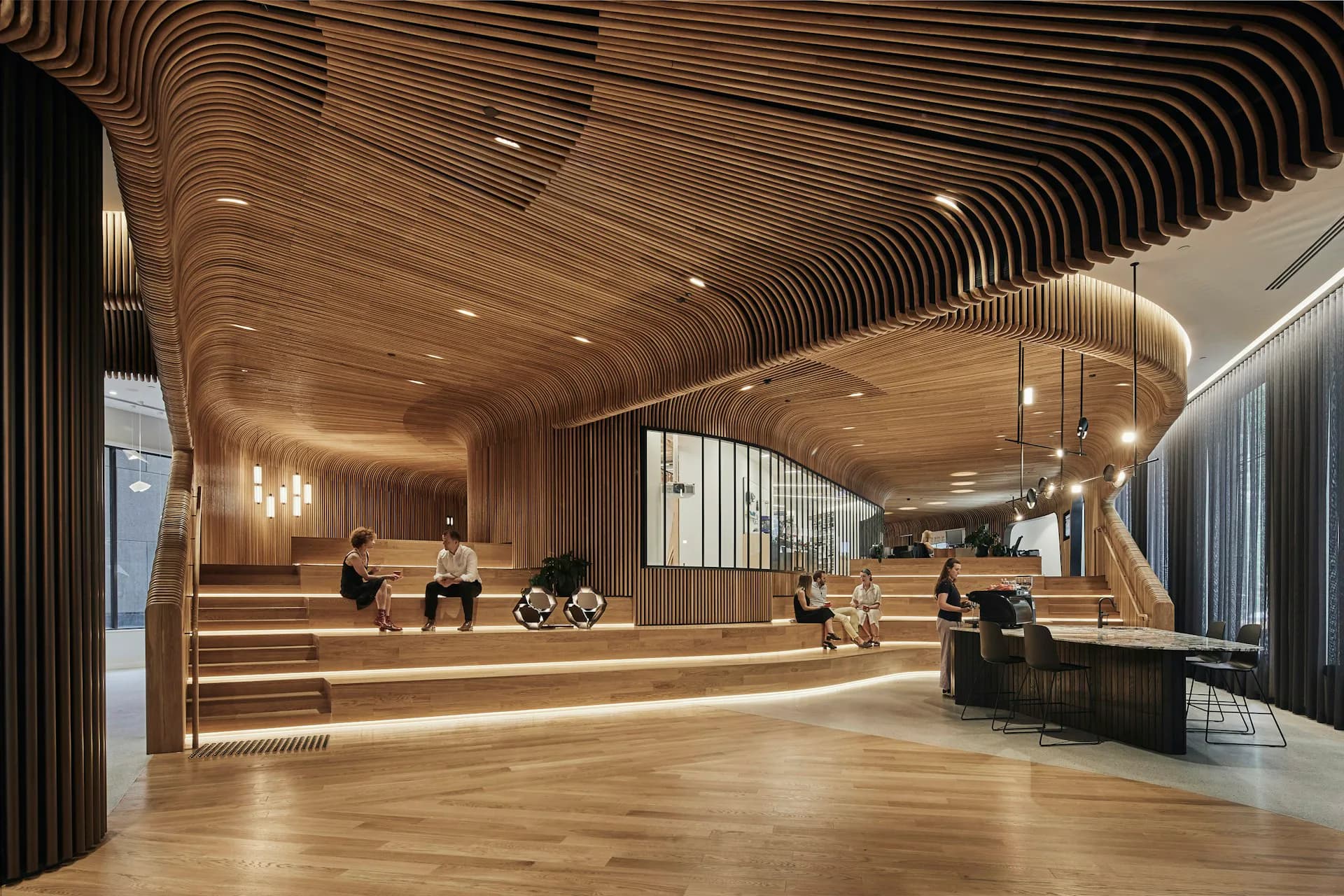 Modern hotel lobby with undulating wooden ceiling, warm lighting, and curved architectural elements by Woods Bagot.