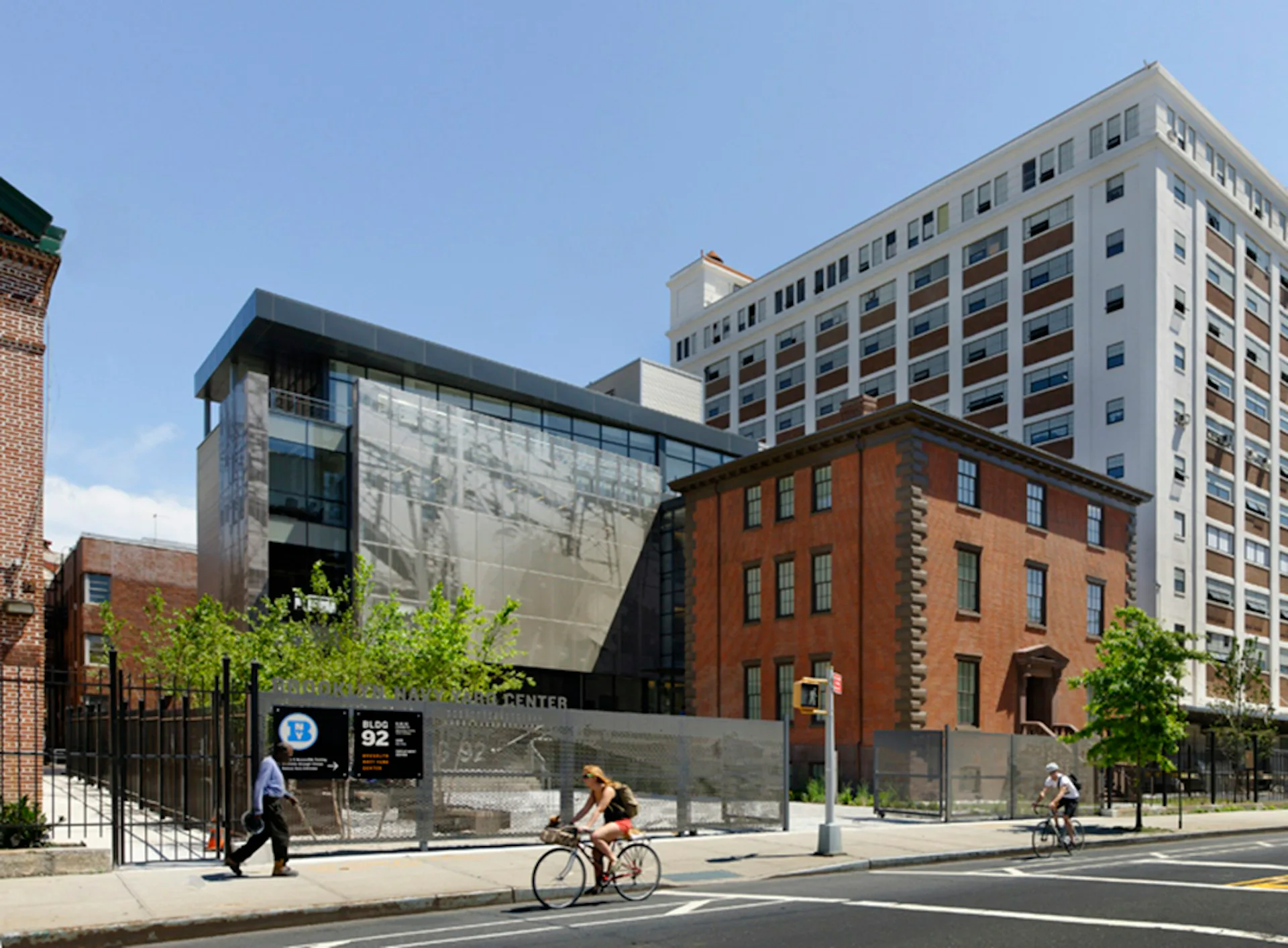 Urban streetscape featuring mixed-use architecture with restored brick building, modern glass structure, and residential tower, designed by Workshop/APD.