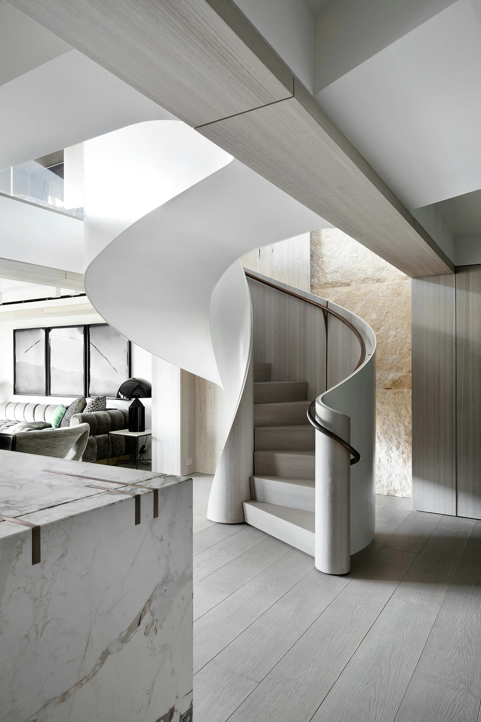 Modern spiral staircase with white curved walls and metal handrail in a minimalist interior with marble and concrete elements by Workshop/APD.
