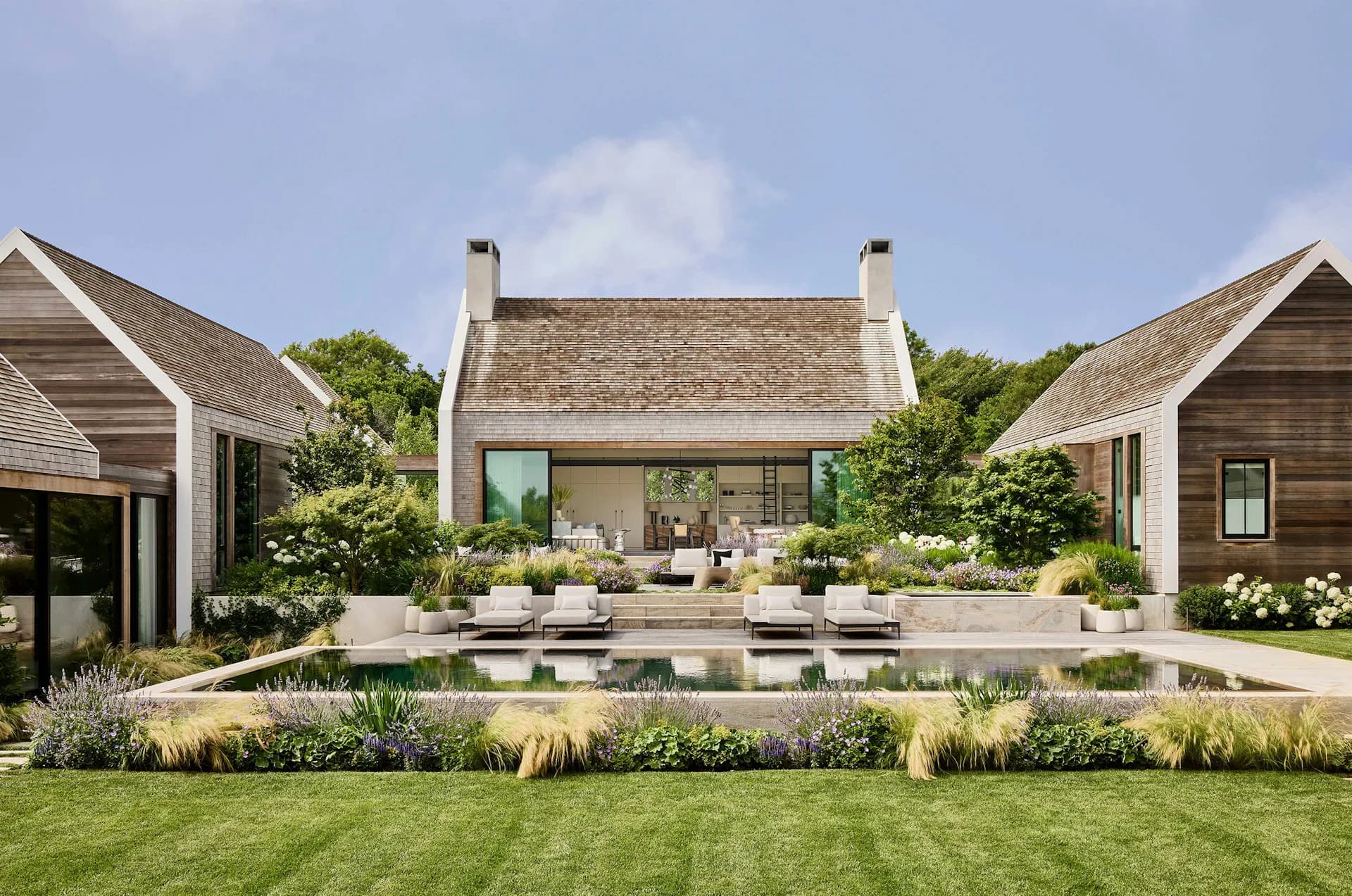 Modern residential courtyard with stone center building, reflecting pool, manicured lawn, and symmetrical side pavilions in neutral tones by Workshop/APD.