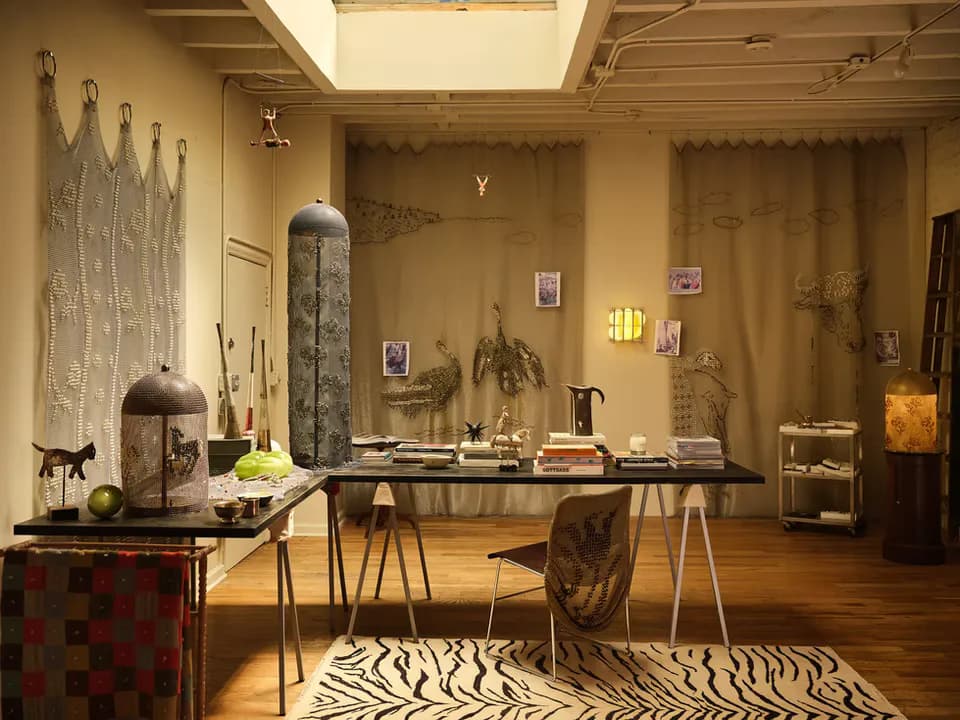 Warm-toned studio interior with wooden desk, zebra-stripe rug, sculptural objects, and ochre walls displaying artwork by Wretched Flowers.