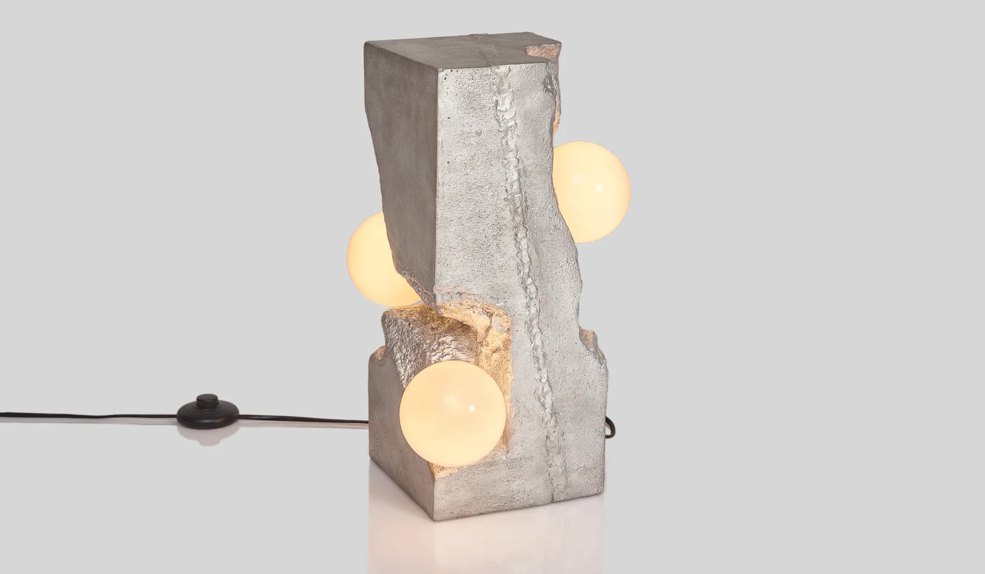 Concrete sculptural lamp with illuminated spheres mounted on its surface, demonstrating minimalist lighting design by Yasanche.