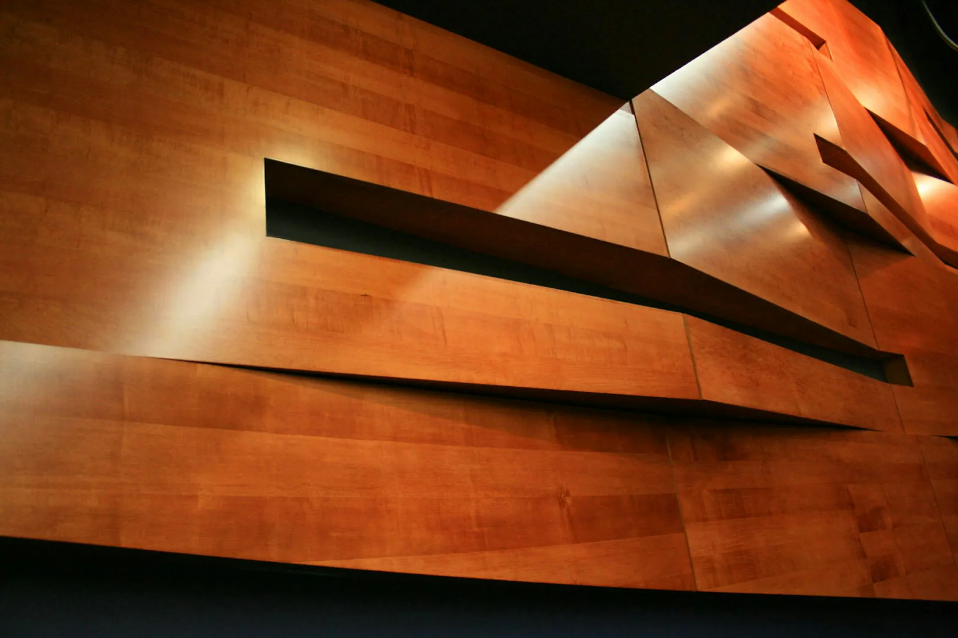 Dramatic interior featuring warm copper-toned wall panels with horizontal black metal bands creating geometric shadows under uplighting, by Yoshihara McKee Architects.