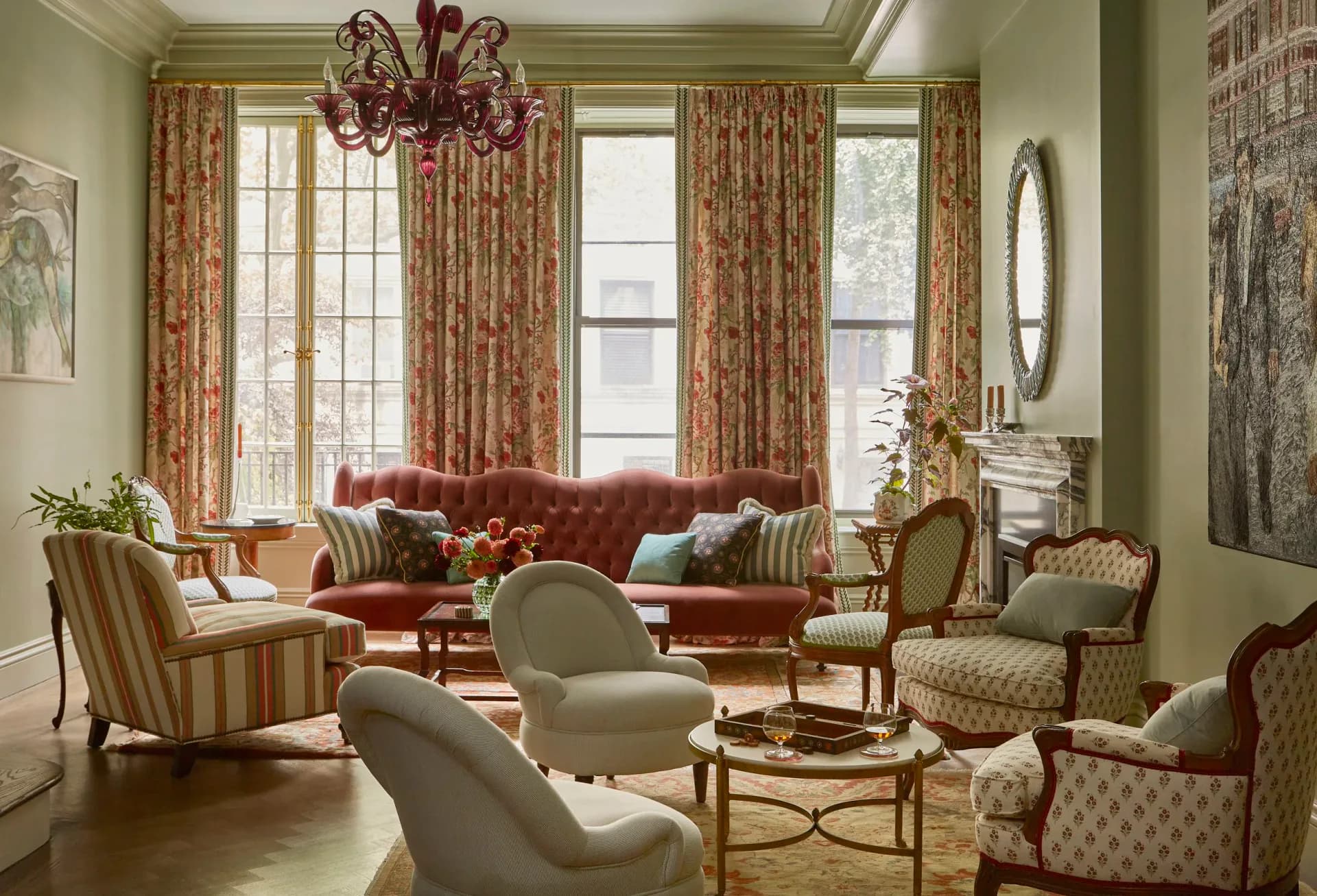 Elegant living room featuring burgundy velvet sofa, striped and patterned upholstered chairs, gold-framed mirror, patterned drapery, and warm green walls by Young Huh Interior Design.