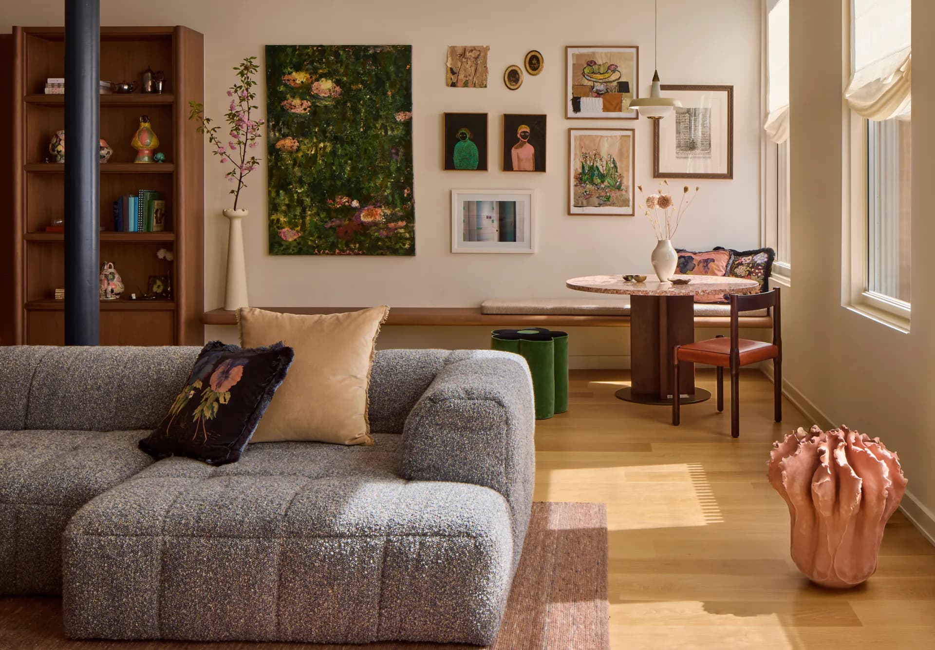 Contemporary living room with curved gray sofa, wooden desk, gallery wall of botanical artwork, green moss installation, and copper vessel on warm wood flooring by Young Projects.