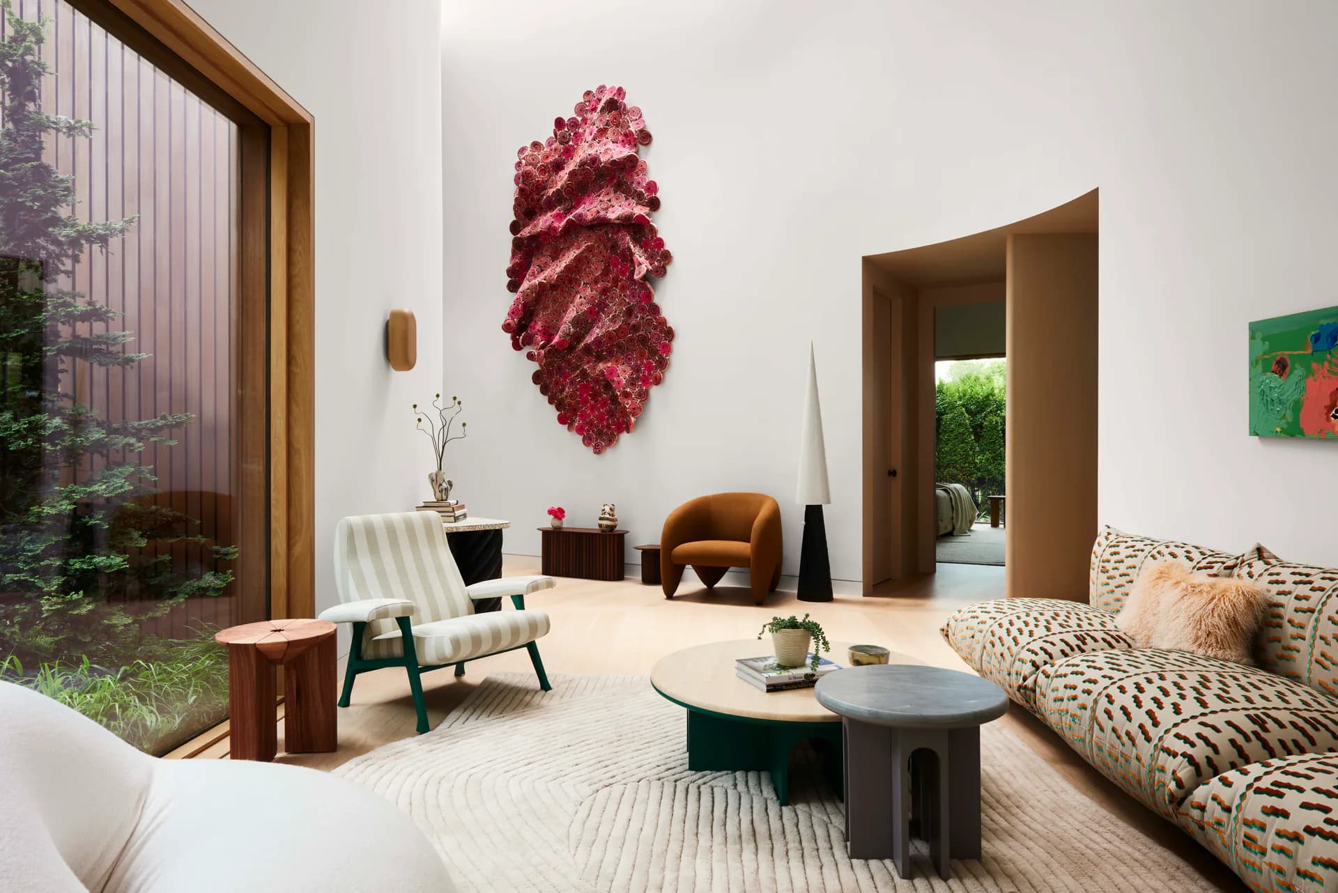 Modern living room with cream and burgundy accents, featuring a sculptural wall installation, angular furniture, and geometric patterns throughout, designed by Young Projects.