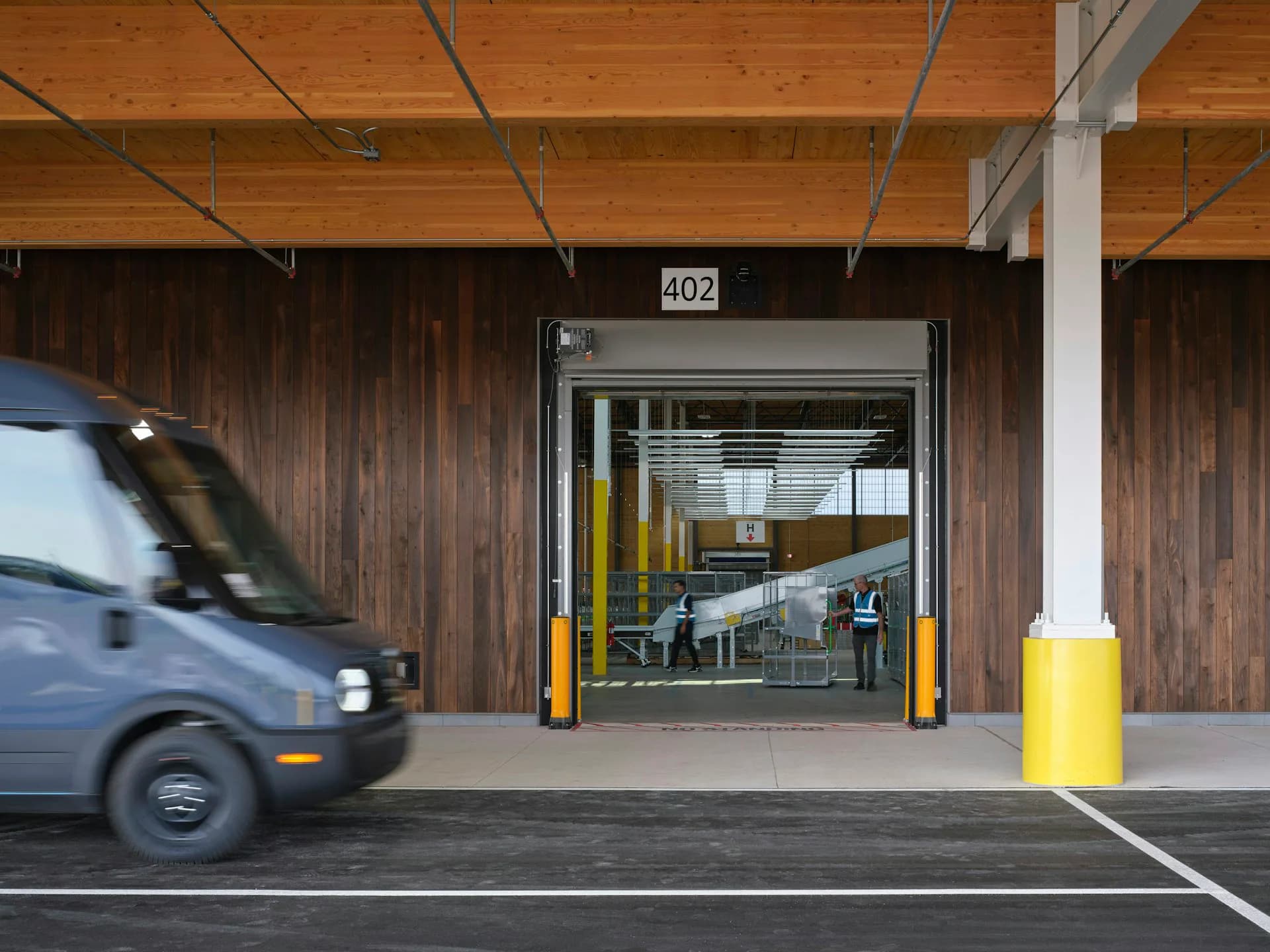 Modern parking garage entrance with wood siding, concrete floor, yellow safety bollards, and exposed ceiling infrastructure by ZGF Architects.