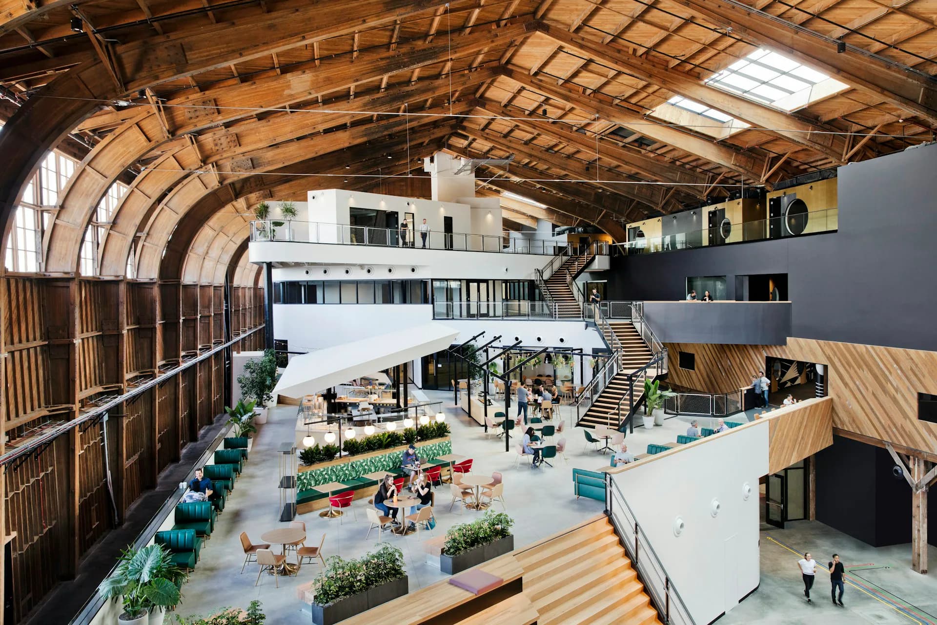 Aerial view of a converted industrial warehouse with barrel-vault wooden ceiling, multi-level open atrium with planted gardens, stairs, and modern furnishings by ZGF Architects.